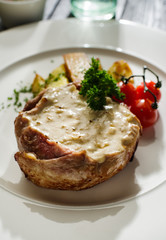 Pork with white mushroom sauce garnished with fried potatoes and cherry tomatoes.