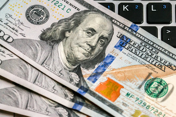 Closeup view of one hundred dollar banknotes lying on the laptop keyboard.