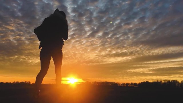 Silhouette of a young happy girl with a backpack holding her hands up the sportswoman. Cheering successful woman hiker open arms on sunset wellness concept.