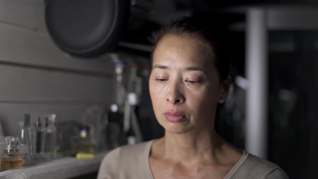 Asian middle aged woman applying face cream in the kitchen