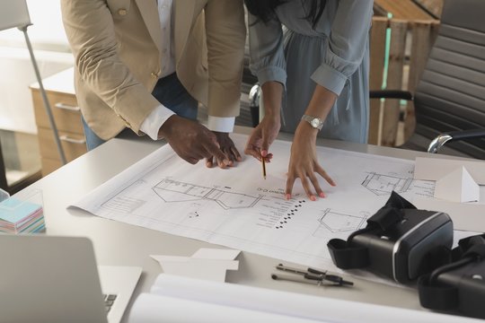 Midsection of architects working over blueprint in office