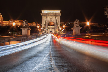 Fototapeta premium Schnelle Autos fahren vorbei - Straßenverkehr nachts auf der Kettenbrücke (Szechenyi Lanchid) in Budapest, der Hauptstadt von Ungarn