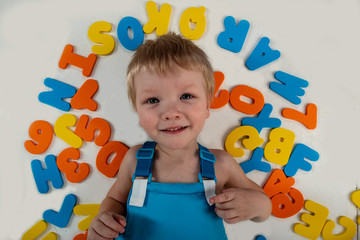 Happy charming Caucasian blond's kid in colored clothes playing with plastic letters. Learning the alphabet, preparing for school. Education for kindergarten and preschool children. White background