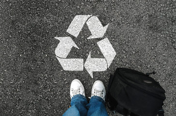  a man with a shoes and backpack is standing next to recycle sign on road asphalt