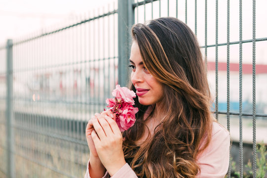 Young charming woman in sweater with flower near grating
