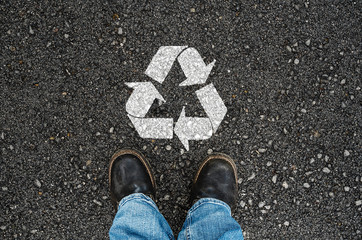 a man with a shoes is standing next to recycle sign on road asphalt