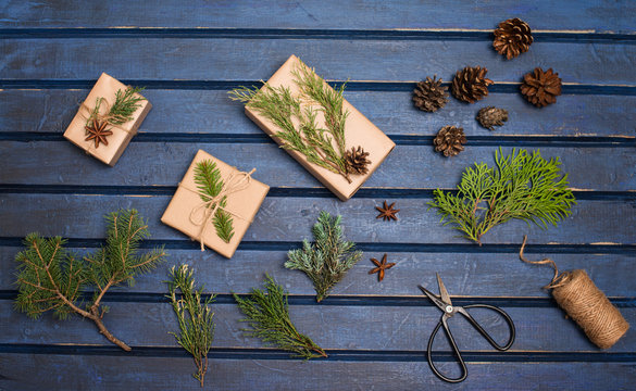 Gift wrapping. Packaging christmas presens. Boxes with fir tree, cedar, juniper, branches. Preparation for holidays. Hand crafted gifts on blue wooden background, natural materials.
