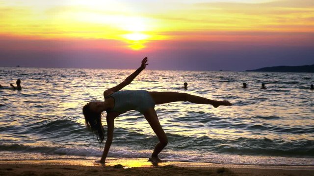 silhouette of a girl at sunset, against the background of the sea, slender leggy girl funny doing gymnastic coups on the sea coast