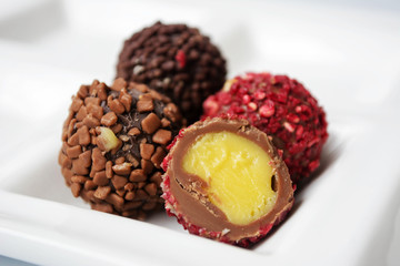 Truffle chocolate collection in white plate. Close up of perfect dessert with creamy filling,  raspberry and chocolate crisps.