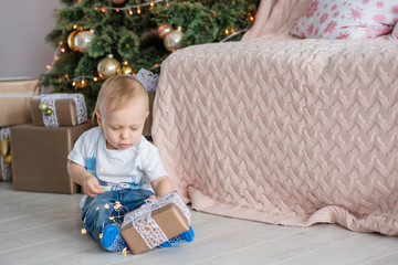 Little blond boy plays with a bright garland at the Christmas tree at cozy home. New Year holiday...