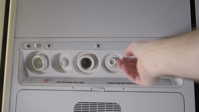 A hand reaching up to open and close the air vent control for the center seat on a commercial passenger airplane