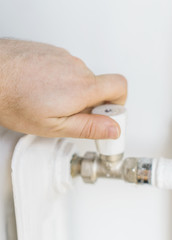 Male hand adjusting thermostat to turn on the radiator heater at home.