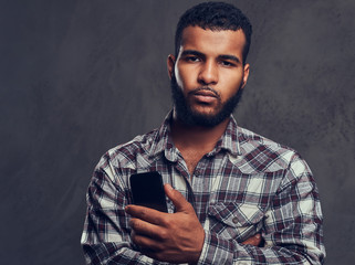 African-American guy with a beard wearing a checkered shirt holding a phone in a studio.