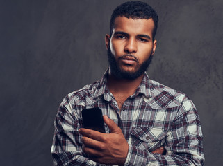 African-American guy with a beard wearing a checkered shirt holding a phone in a studio.