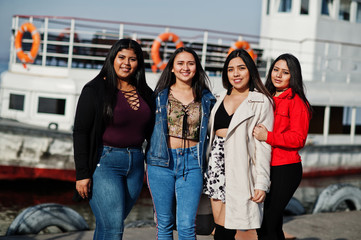 Group of four happy and pretty latino girls from Ecuador posed against boat.