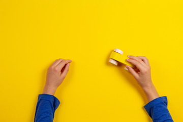 Child hands playing with wooden toy car on yellow background, top view