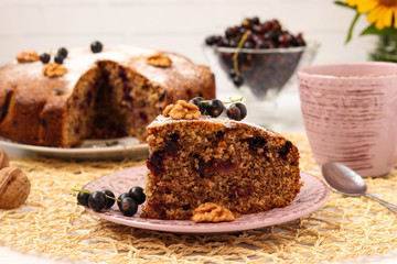 Homemade pie with black currant and walnuts is located on a plate on a white background.  In the foreground is a piece of cake