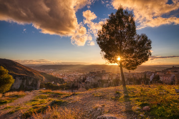 The rays of the setting sun coming through a tree at the top castle area of Cuenca Spain overlooking the entire town and the mountains and city - Powered by Adobe