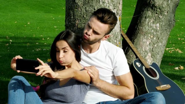 Happy couple taking a picture of themselves with a smartphone on a green lawn.