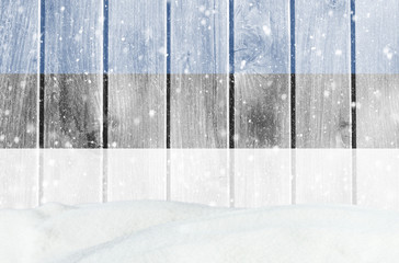 Christmas winter background with wooden wall, falling snow, snowdrift and Estonian flag