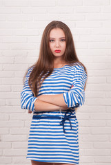 Portrait of a brown-haired girl in a stripped vest against a white brick wall.