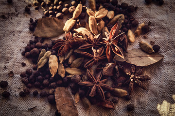 Scattered black peppercorn, beans, cinnamon and bay leaves on linen fabric