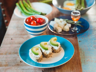 brunch of curd cheese sandwiches with avocado, tomatoes, brie and honey, boild green asparagus and fried eggs on the plate