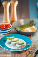 brunch of curd cheese sandwiches with avocado, tomatoes, boild green asparagus and fried eggs on the plate