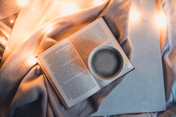 Open book with cup of coffee in bed at night. Top view.