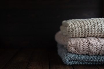 Obraz na płótnie Canvas Stack of cozy knitted sweaters on dark wooden background. Autumn-winter concept,knitted wool sweaters. Pile of knitted winter clothes, sweaters, knitwear, space for text.