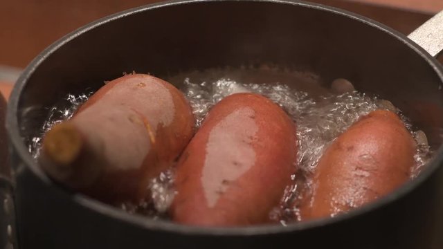 Close up on sweet potatoes in a black pot of boiling water on a stove.