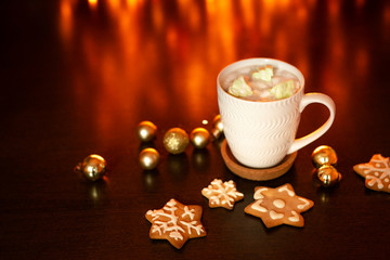 White cup of cocoa or coffee with hot chocolate and marshmallows and gingerbread cookies on the dark brown table and background with golden bokeh. Christmas holiday concept, free space for text