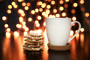 White cup of cocoa or coffee with hot chocolate and marshmallows and gingerbread cookies on the dark brown table and background with golden bokeh. Christmas holiday concept, free space for text