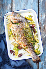 Frisch gegrillte griechische Dorade mit Perperoni und Kalamata Oliven als Draaufsicht in einer weißen Bratreine 