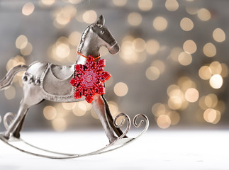 Christmas silver vintage horse with red wooden snowflake on neck against festive bokeh background,...