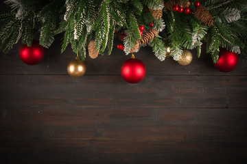 Christmas background with fir tree green branches, greeting card with decoration in red and golden colors on dark brown wooden board, copy space