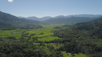 Fototapeta na wymiar Mountain valley with village, farmland, rice fields. Aerial view of Mountains with green tropical rainforest, trees, jungle with blue sky. Philippines, Luzon.