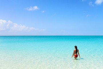 Beach luxury travel getaway resort bikini woman swimming in idyllic turquoise ocean water in paradise destination.
