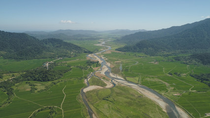 Mountain valley with river, farmland, rice fields. Aerial view of Mountains with green tropical rainforest, trees, jungle with blue sky. Philippines, Luzon.