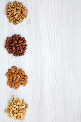 Assortment of nuts (cashew, hazelnuts, walnuts, almonds) on white wooden surface. Top view. Space for text.