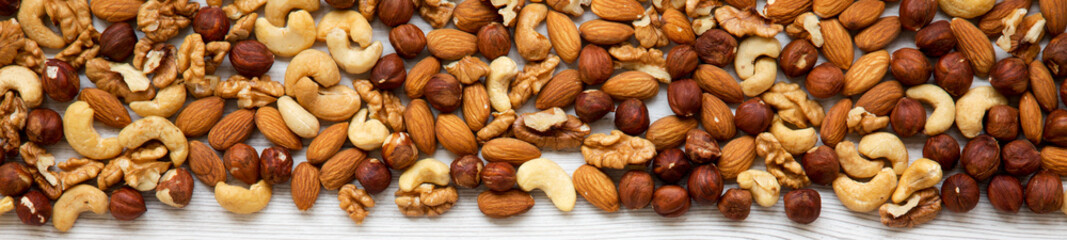 Assorted mixed nuts (cashew, hazelnuts, walnuts, almonds) on white wooden surface, overhead view....