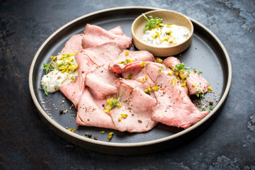 Traditional lunch meat with sliced cold cuts roast beef and remoulade as closeup on a modern design plate on black background