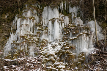 Icicles of an overfrozen spring dripping down a limestone cliff