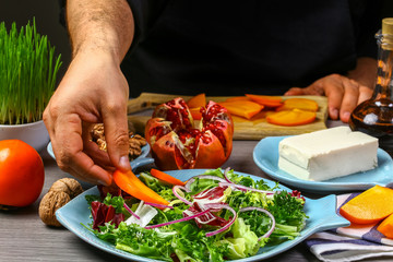 Close up of a chef hands preparing salad with persimmon, pomegranate, nuts and feta cheese. The concept of cooking recipe