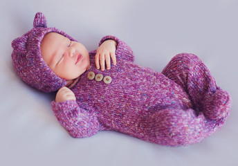 cute newborn baby girl in purple knitted overall is sleeping peacefully