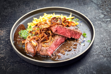 Traditioneller deutscher Zwiebelrostbraten aufgeschnitten mit Röstzwiebel und schwäbische Spätzle als closeup auf einem Modern Design Teller mit brauner Sauce 