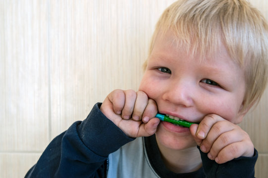 beautiful blond boy holds colored pencil in his teeth. Drawing lessons in group of preschoolers
