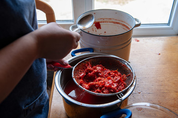woman cook prepares tomatoes in a saucepan, rubs through a sieve and prepares tomato juice. Female hands closeup.