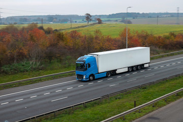 Refrigerated lorry in motion on the road against autumn landscape