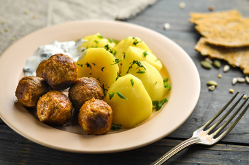 Swedish meatballs with potatoes. Garlic sauce, fresh herbs and cereal tortilla. Dish of national cuisine on a wooden table.